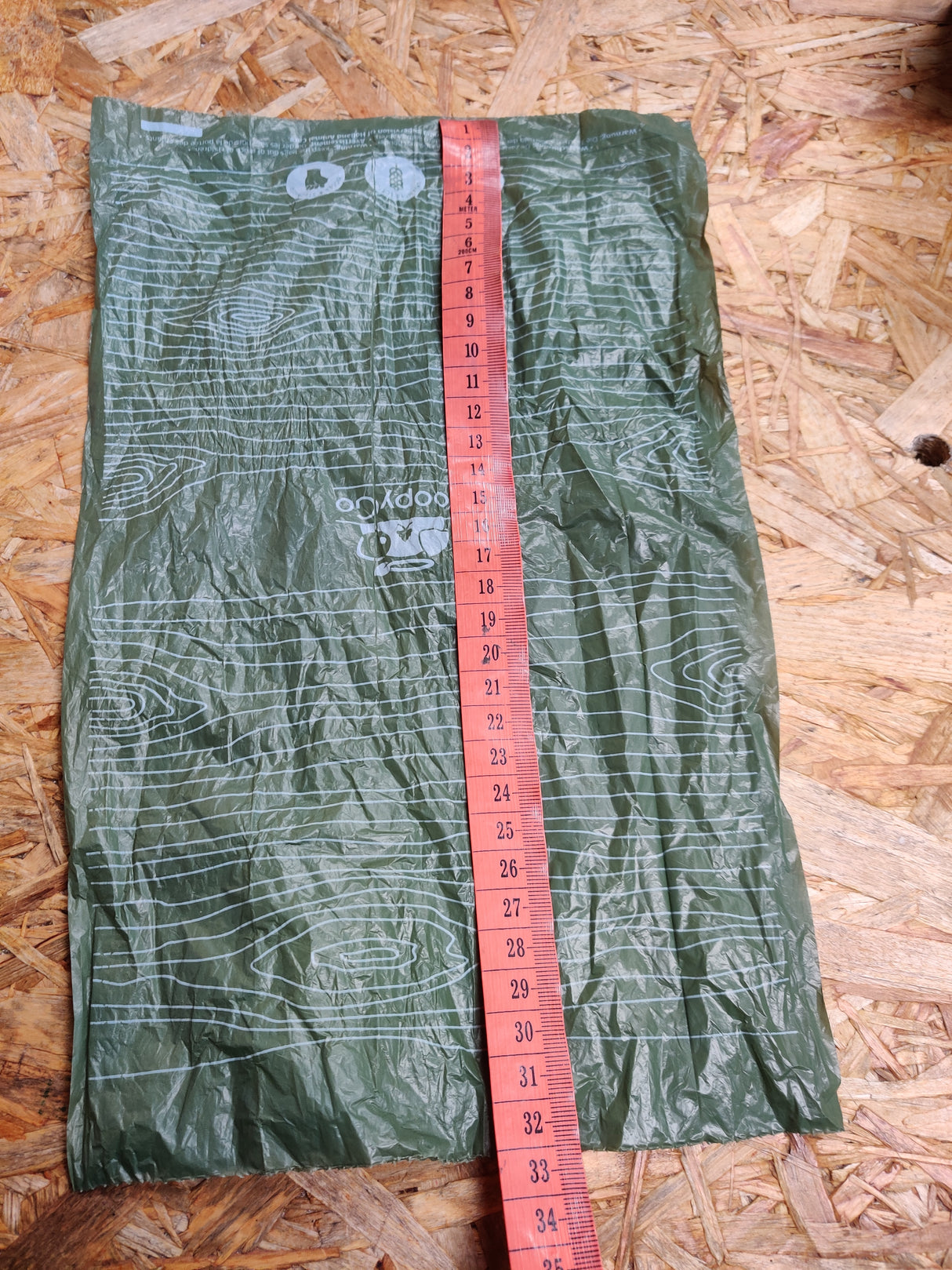 En grøn taske med et målebånd og Høm Høm hundeposer, miljøvenlige fra PoopyGo 300 poser logo på.