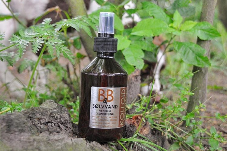 En flaske B&B Økologisk spray med en hund i baggrunden, indeholdende B&B Sølvvand mod sår, rifter, hotspots, kløe, skæl, hævelse mm til hunde.