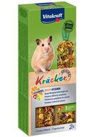 En hamster, der glad gumler på Vitakraft Kräcker, tandslibende stænger til hamster i en kasse mad.