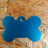 Beskrivelse: Et Hundetegn, lyseblå, formet som kødben fra Os med kæledyr på en træoverflade.