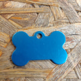 Et Hundetegn, lyseblå formet som kødben id tag med gravering på en træoverflade af mærket Os med kæledyr.