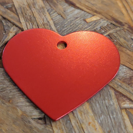 Et "Os med kæledyr" hjerteformet metalmærke med rød diamantindgravering på en træoverflade.