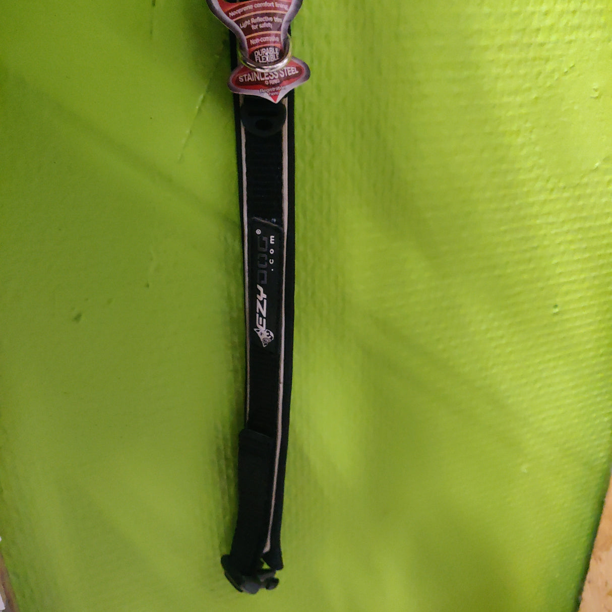 Et EzyDog halsbånd - Sort, et sort og rødt hundehalsbånd, hængende på en grøn væg.