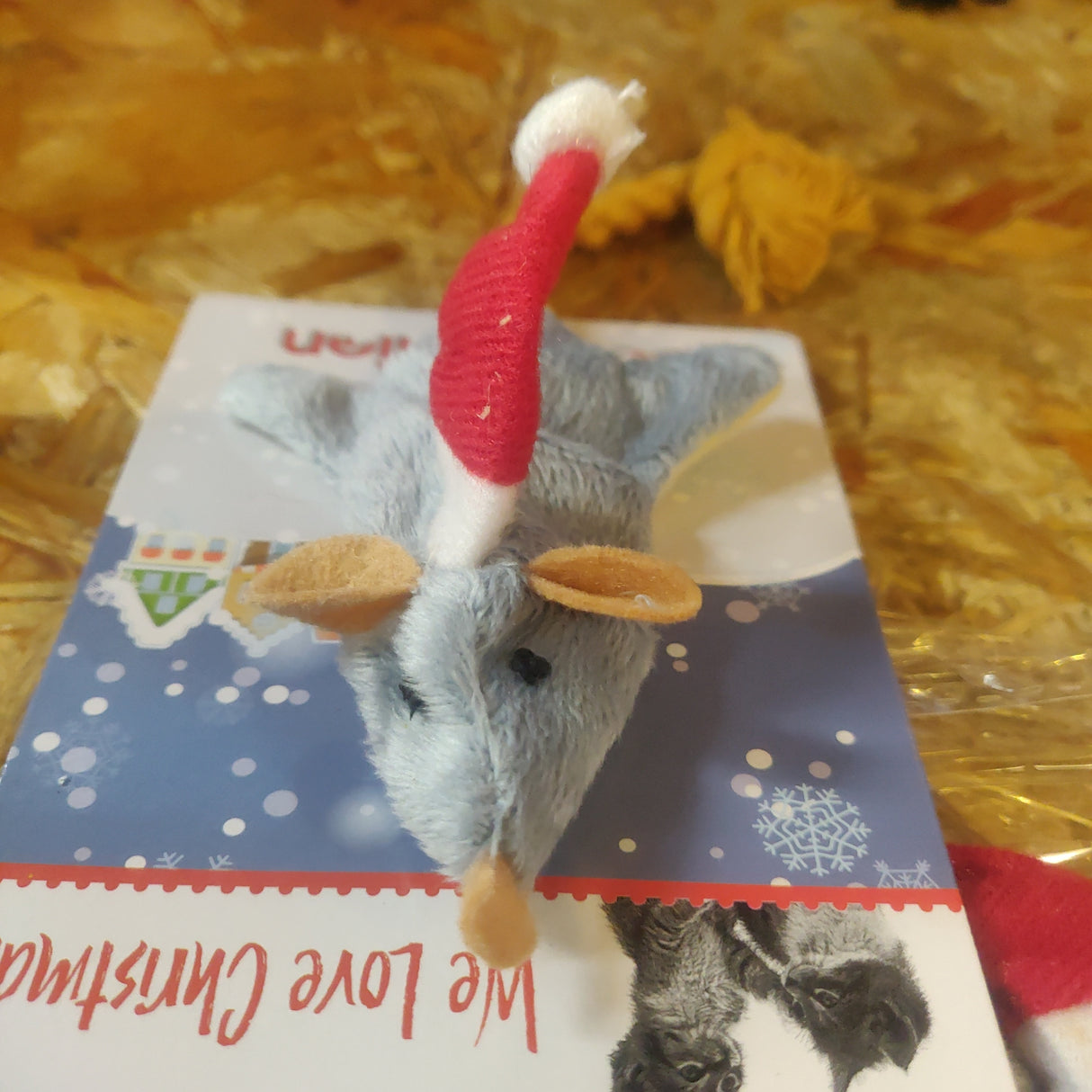En Good Boy kattelegetøj-mus klædt i en nissehue sidder oven på et kort med gaver-tema.