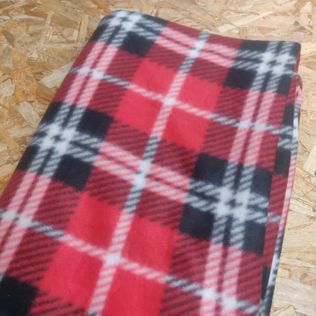 En rød og sort plaid Trixie fleecetæppe oven på et trægulv.