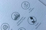 Et nærbillede af et stykke papir med forskellige symboler på, der viser den højkvalitets Hundeseng Fantail Snooze Botanical Green en lækker grå/grøn seng med høj kant fra Fantail.