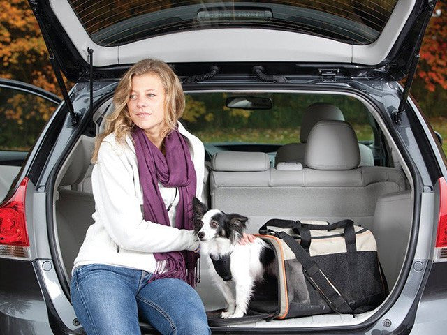 En kvinde sidder i bagagerummet på en bil med sin hund i en Qpet Transporttaske, flygodkendt - Kurgo Wander-bærer.
