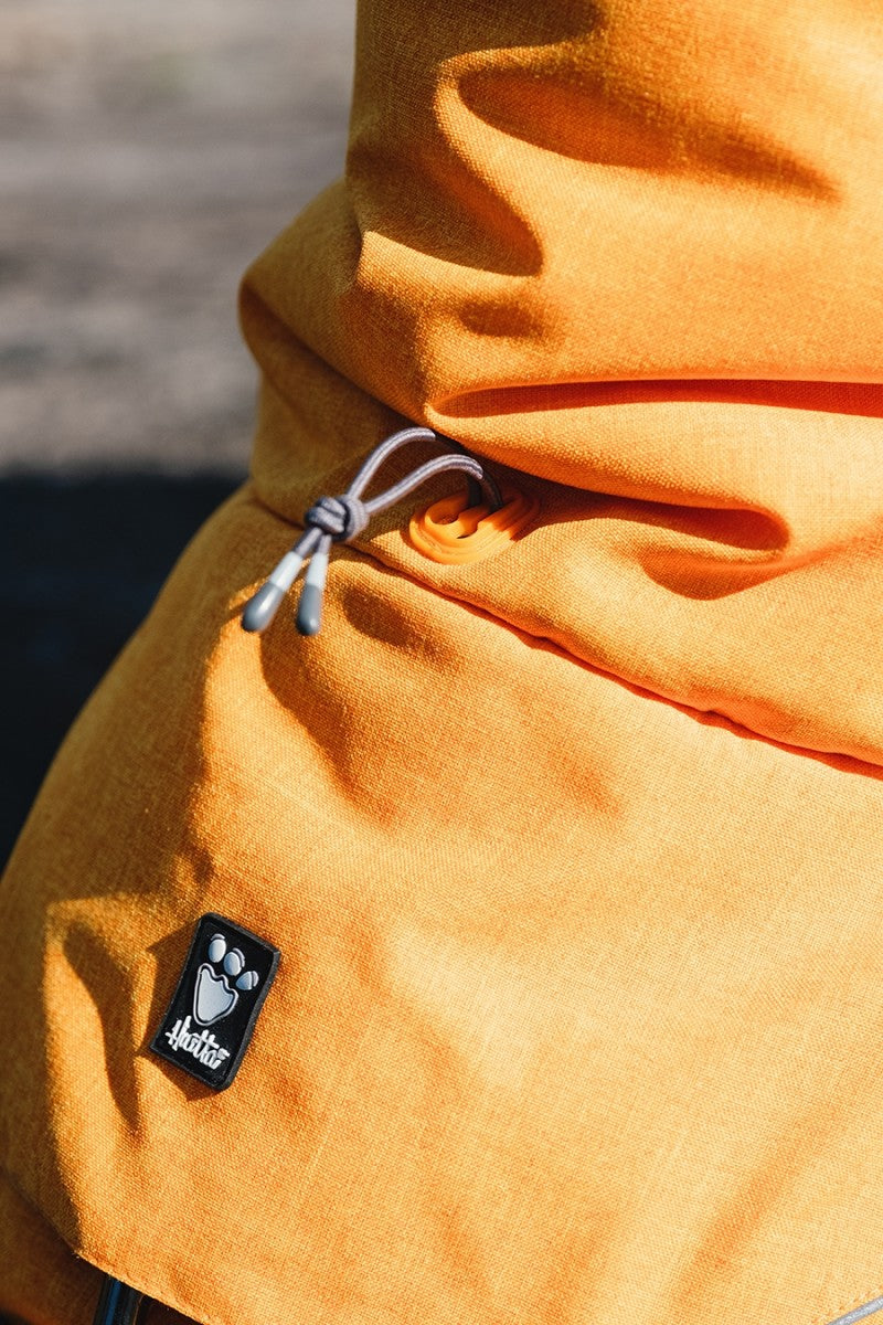 Bagsiden af en kvindes orange jakke med logo på, perfekt til ekspeditioner i koldt vejr, som Hurtta - Expedition Parka Grå (Blackberry) Vinterdækken til hunde.