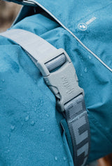 En blå Hurtta-rygsæk med en vandtæt rem fastgjort til, nærmere bestemt Regndækken fra Hurtta, Monsoon Jakke Blackberry (sort).