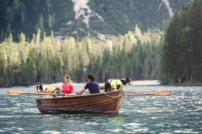 En mand og kvinde ror en båd med deres hunde, som er iført komfortable og velsiddende Hurtta-redningsveste designet til svømmesikkerhed.